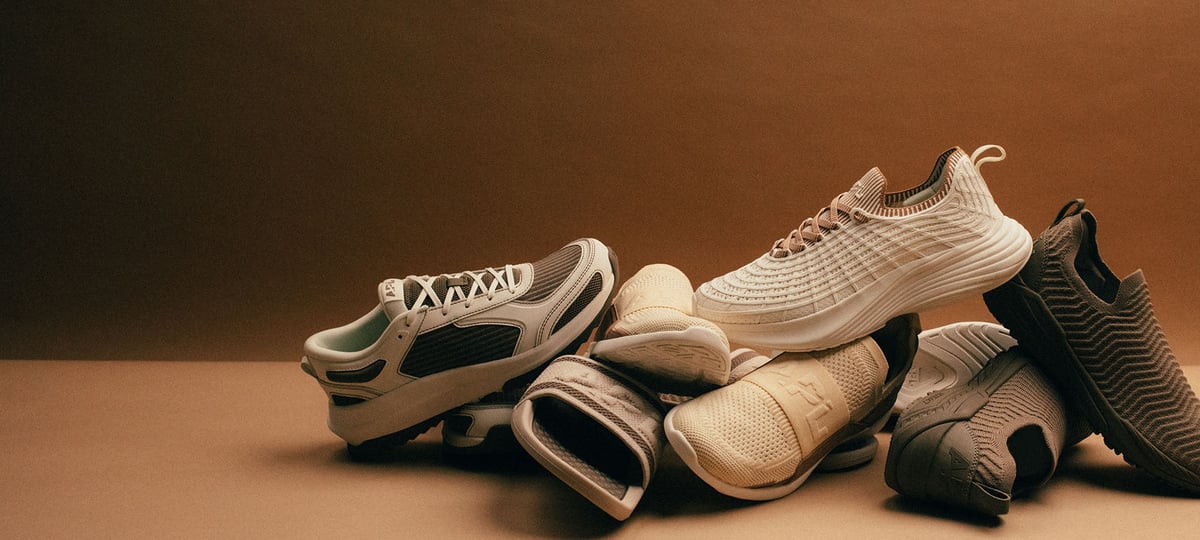 APL athletic footwear in neutral tones against a warm brown background