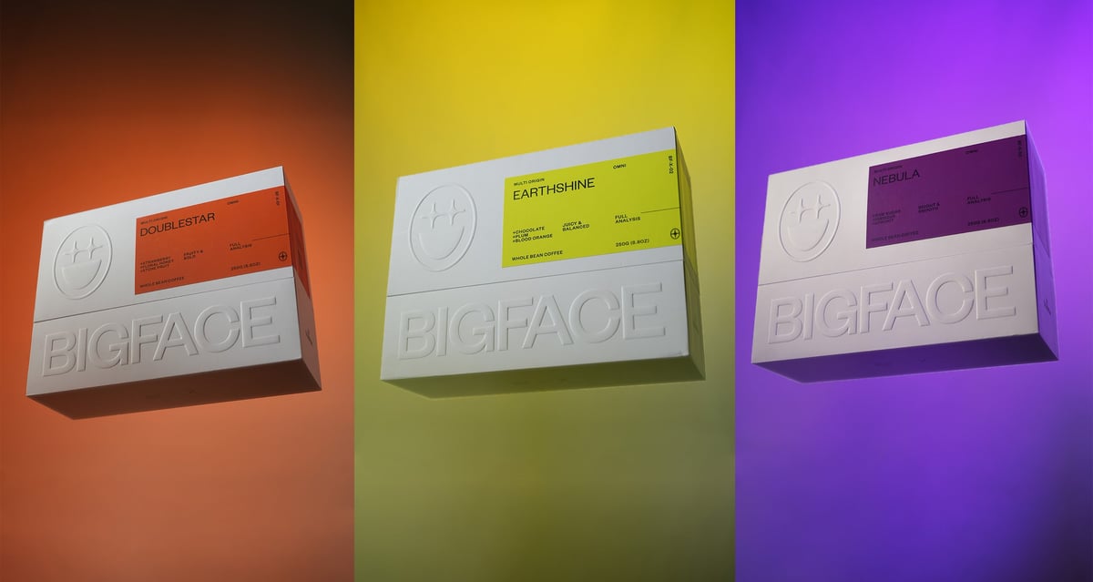 Three colorful BIGFACE coffee boxes on orange, yellow, and purple backgrounds
