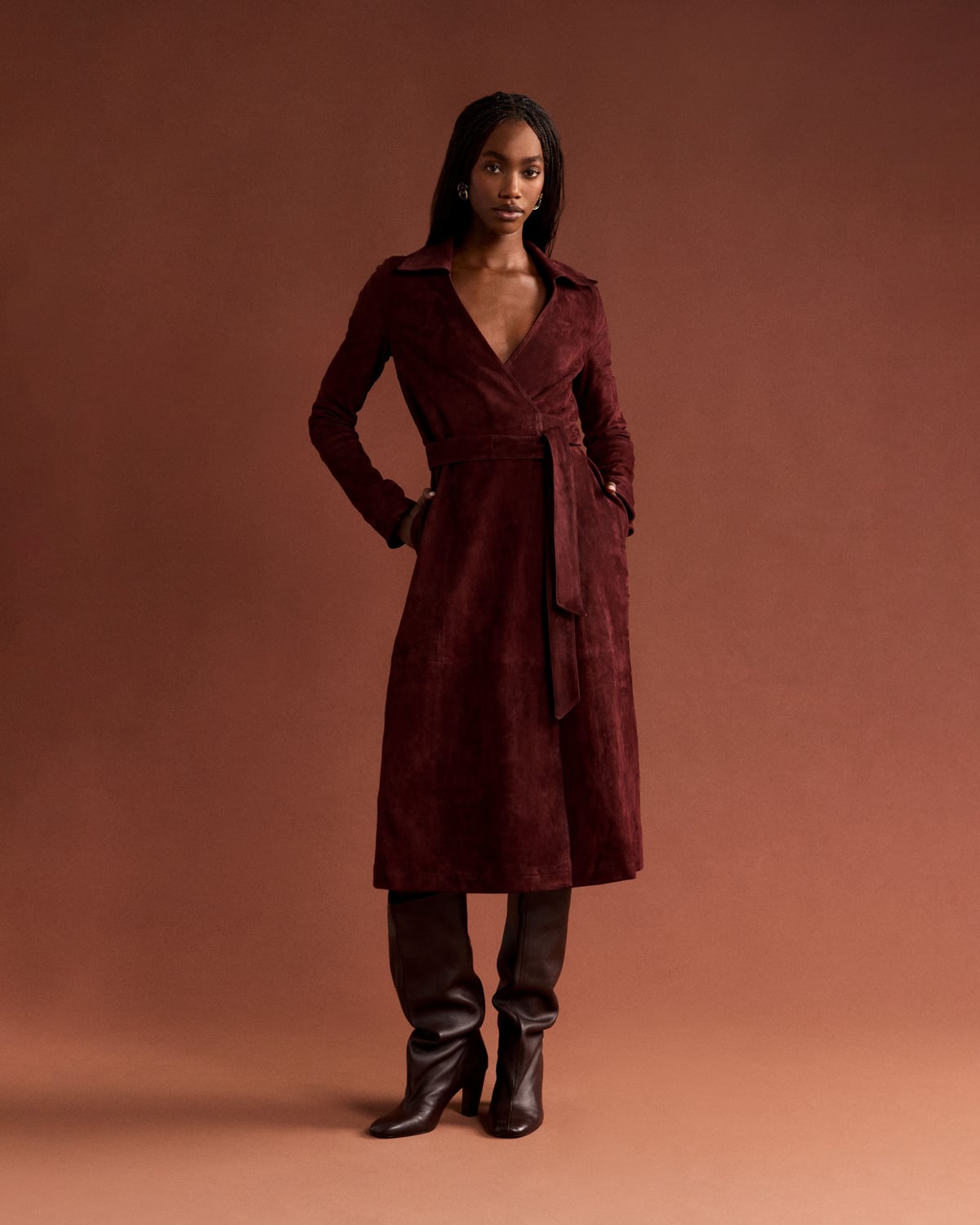 A model wearing a burgundy wrap dress and boots in a warm-toned studio