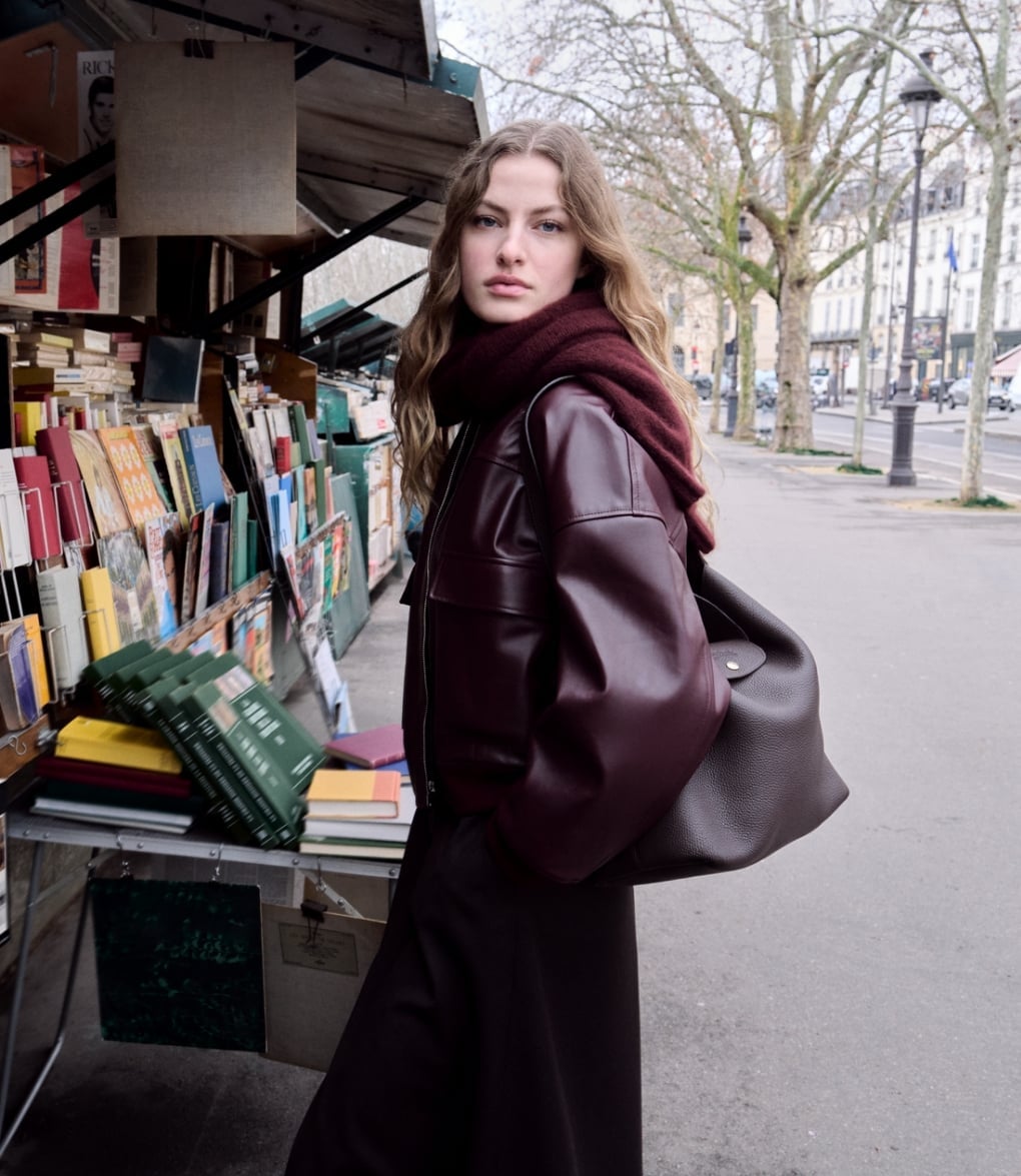 A model carrying a dark leather shoulder bag beside a Paris bookstall