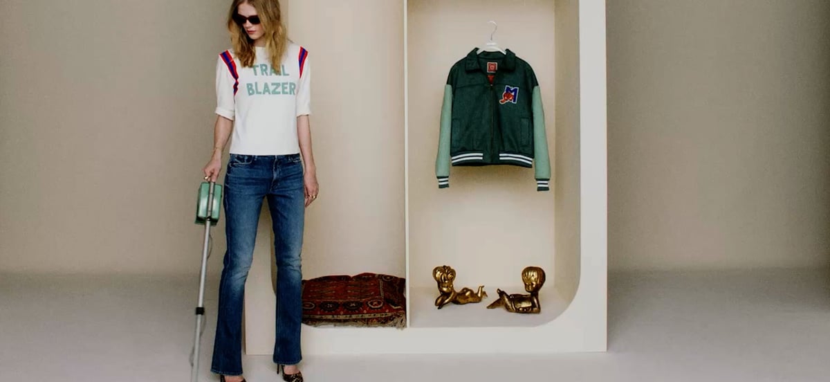 A model in jeans and a white tee beside a recessed display with a green jacket