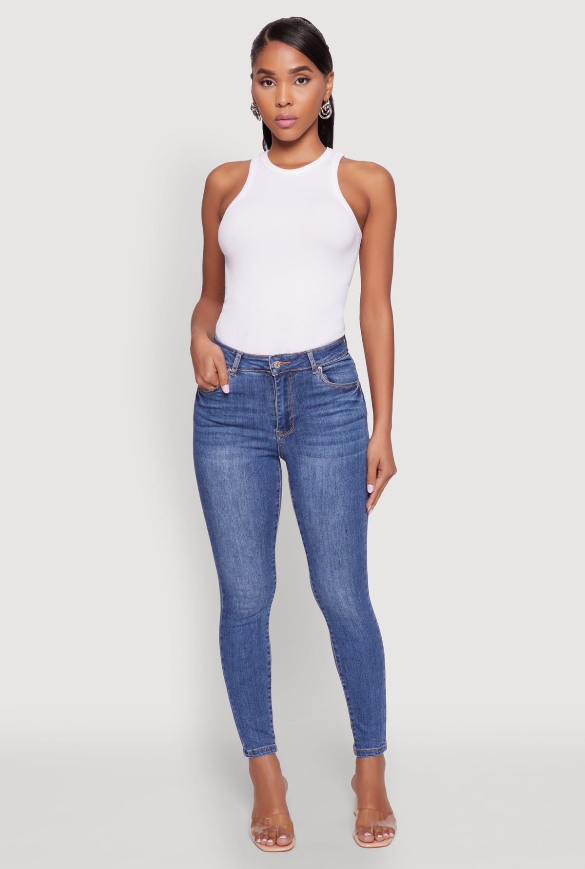 A model wearing a white sleeveless top and blue jeans from Rainbow Shops