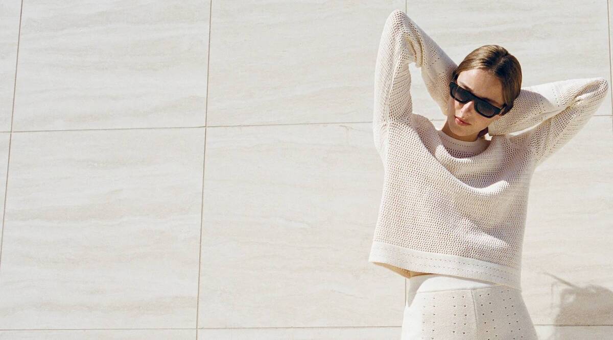 A model wearing a cream knit outfit against a pale stone wall